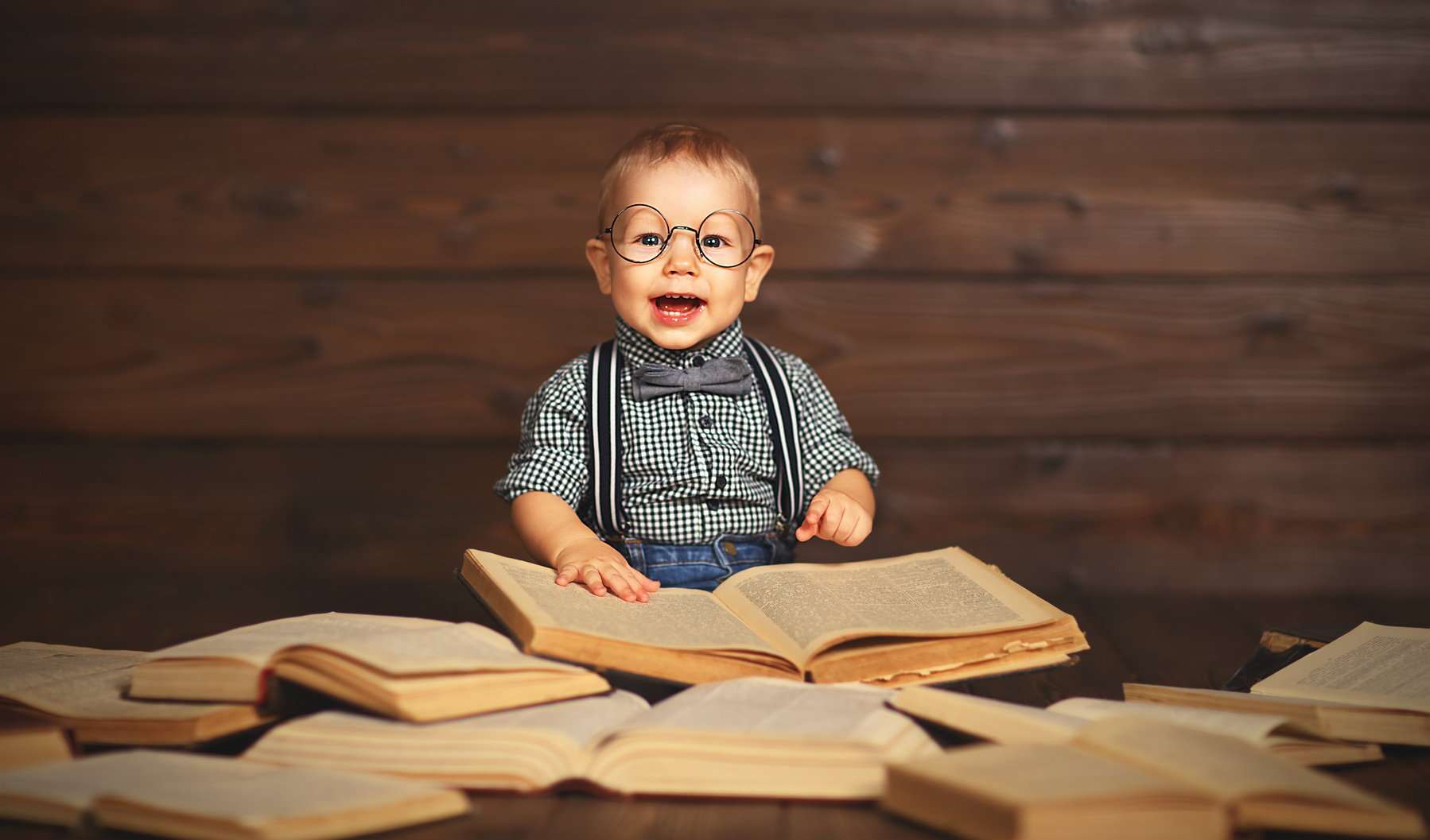 funny baby with books in glasses on a wooden background