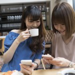 Women are chatting at a cafe while watching smartphones